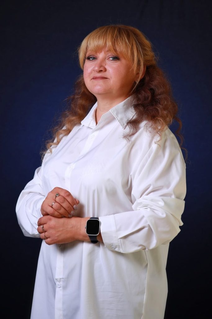 Женщина с вьющимися светлыми волосами в белой оверсайз-рубашке, на синем фоне